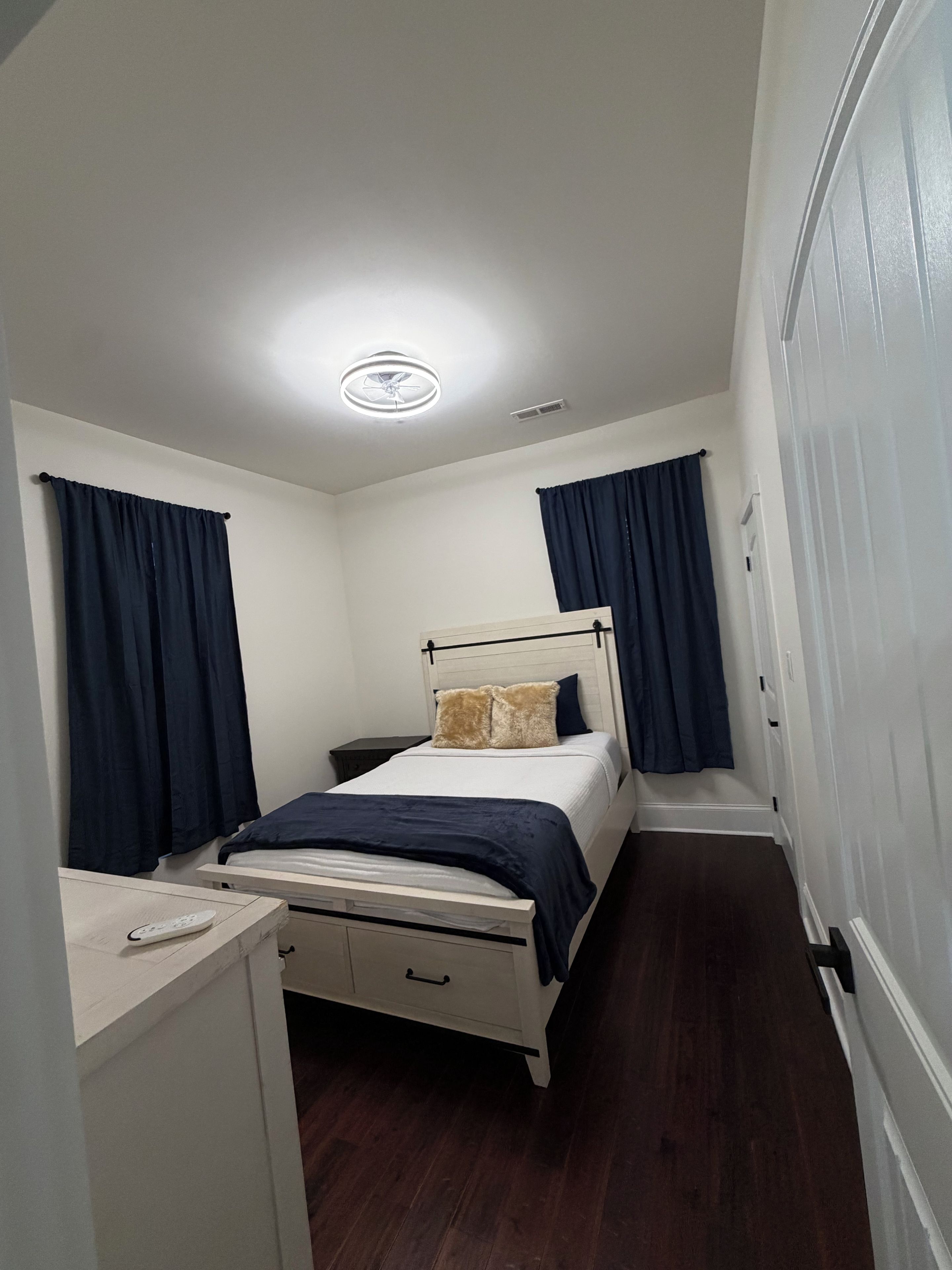 A small, narrow room with a bed, a desk, and a wardrobe.