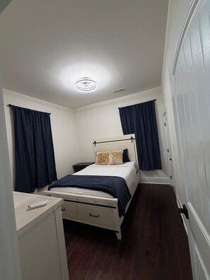 A small, narrow room with a bed, a desk, and a wardrobe.