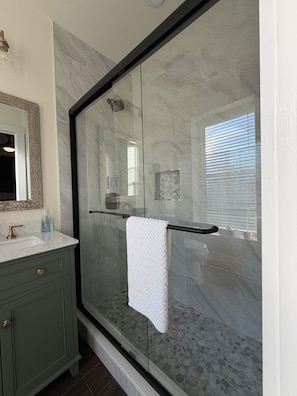 A bathroom with a glass-enclosed shower, a marble-tiled wall, a green vanity, and a white towel hanging on a towel rack.