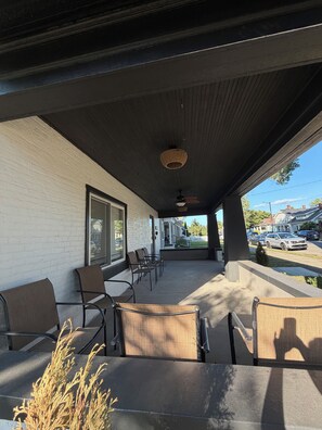 A covered outdoor seating area with chairs and a table, a brick wall, and a view of a residential street.