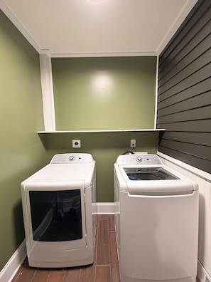 A laundry room with two front-loading washing machines and a dryer, green walls, and a wooden floor.