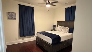Quarto com cama, ventilador de teto e cortinas escuras.