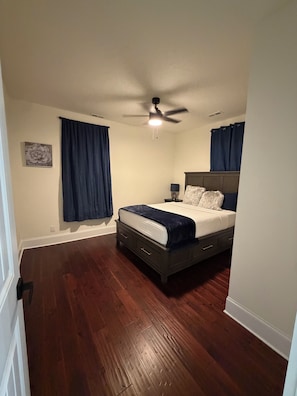 A bedroom with a bed, a ceiling fan, and dark curtains.