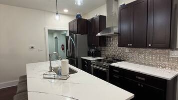 A modern kitchen with dark cabinets, a white marble island, stainless steel appliances, and pendant lighting.