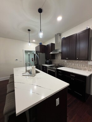 A modern kitchen with dark cabinets, a white marble island, stainless steel appliances, and pendant lighting.