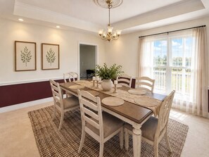 Ein Esszimmer mit einem langen Tisch, Stühlen, einer Chandelier und Blick durch große Fenster.