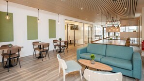 Ein modernes Interieur mit einem blauen Sofa, Holztischen und -stühlen. Eine Glastrennwand und eine Holzwand mit Pendelleuchten sind ebenfalls vorhanden.