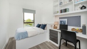 Ein Schlafzimmer mit Bett, Schreibtisch, Stuhl, Fenster und Bücherregal.
