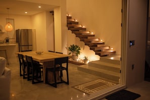 Eine moderne Küche mit Einbaukühlschrank, einem Esstisch mit Stühlen und einer Treppe mit integrierter Beleuchtung.