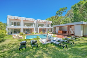 Ein modernes, zweigeschossiges Haus mit Swimmingpool, Sitzgelegenheiten im Freien und einem gepflegten Rasen.