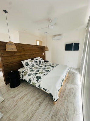 Ein modernes Schlafzimmer mit einem Holz-Kopfteil, einem Bett mit Bettwäsche in Blättermuster, einer Pendelleuchte, einer Klimaanlage und einem Deckenventilator.