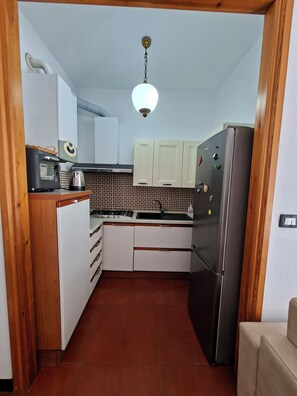 A compact kitchen with white cabinets, a stainless steel refrigerator, a microwave, and a gas stove. - Oasi Nel Verde Just a few dozen meters from the sea and close to downtown (Rapallo)