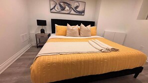 Cama bem arrumada com colcha amarela, cabeceira preta e várias almofadas.