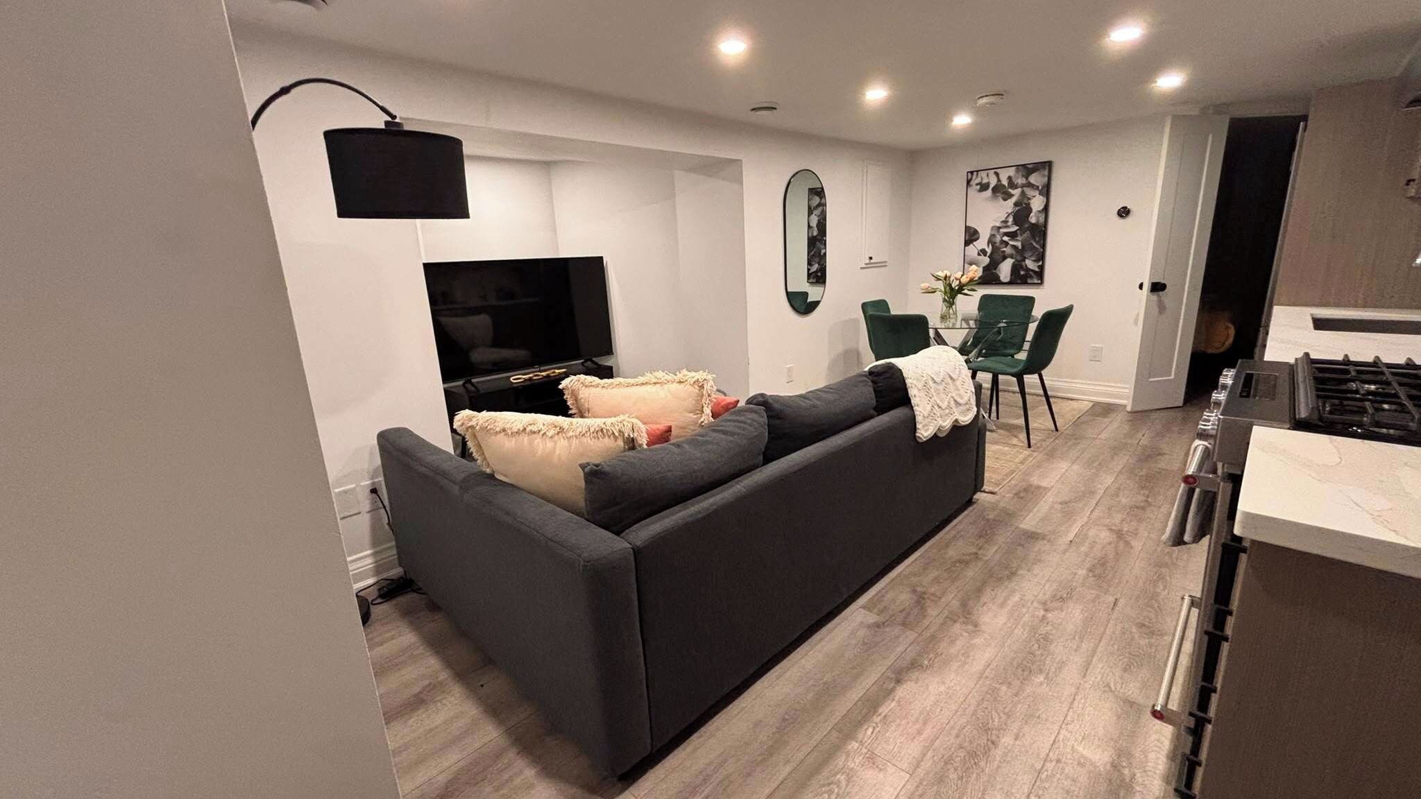 A modern living room with a sofa, a flat-screen TV, and a dining area with chairs.