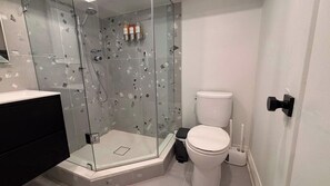 Casa de banho com chuveiro envidraçado, sanita e um lixo preto.
