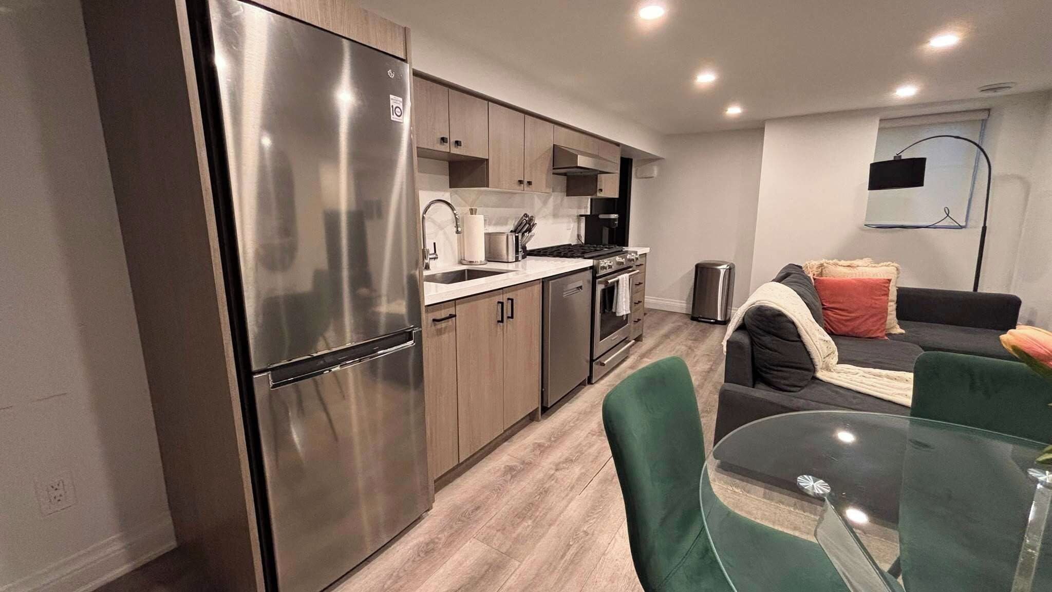 A modern kitchen with stainless steel appliances, wooden cabinets, and a dining area with a glass table and green chairs.