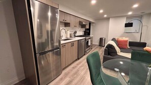 A modern kitchen with stainless steel appliances, wooden cabinets, and a dining area with a glass table and green chairs.