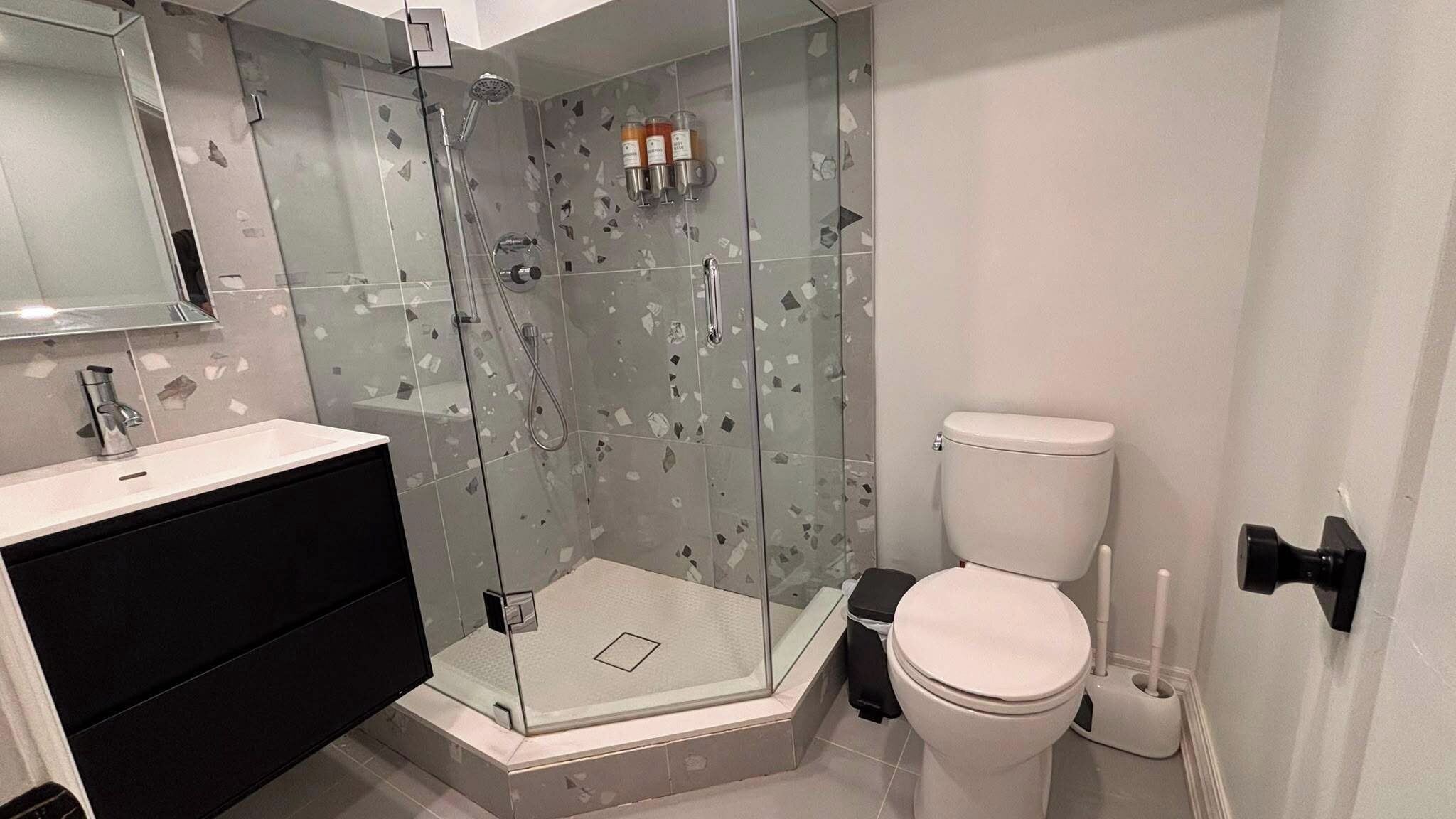 A modern bathroom with a glass-enclosed shower, a white toilet, and a black vanity.