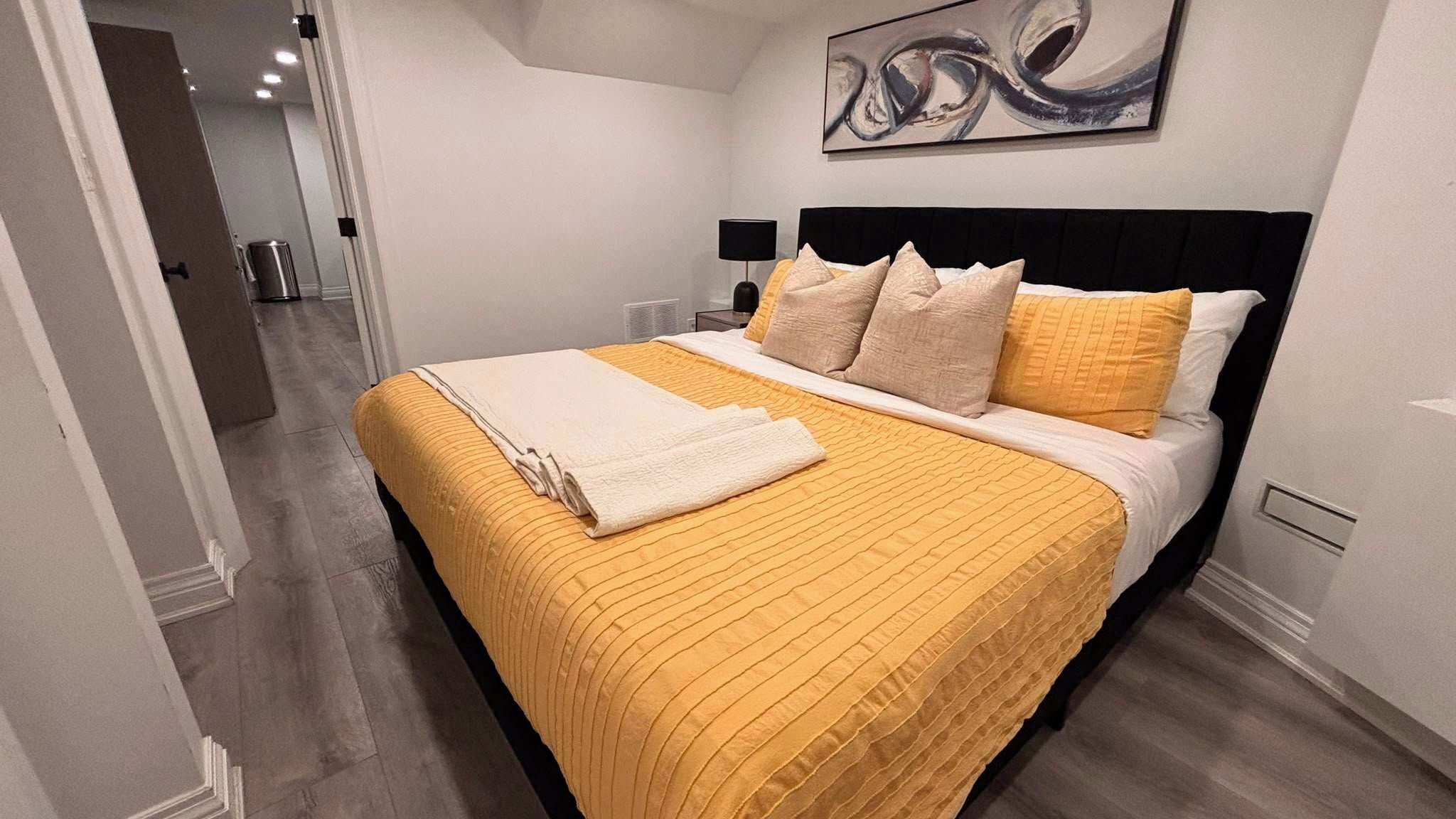 A hotel room with a bed, a nightstand, a lamp, and a painting on the wall.