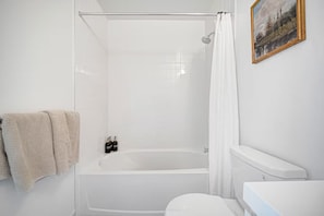 Et badeværelse med badekar, toilet og bruseforhæng.