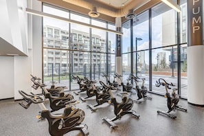 Et fitnessrum med flere spinningcykler stillet op i rækker, store vinduer og udsigt til bybilledet.