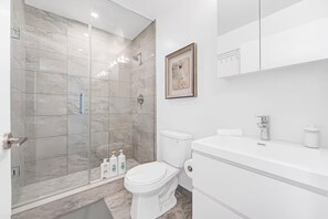 Et moderne badeværelse med en glasafskærmet brusekabine, toilet og vask med et spejl over.