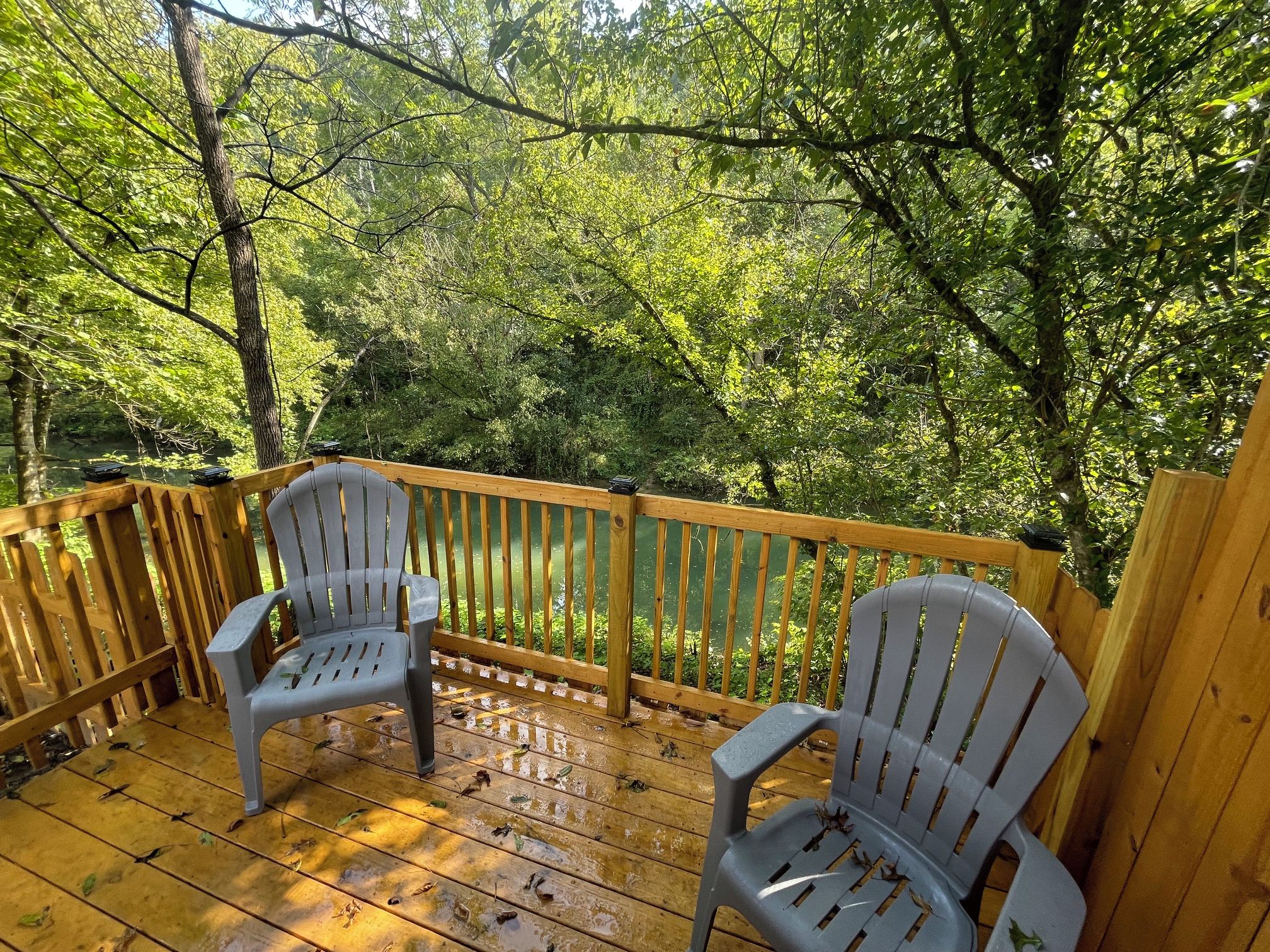 Une terrasse en bois avec deux chaises et une rambarde donnant sur une zone boisée.