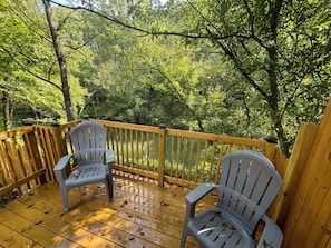 A wooden deck with two chairs and a railing overlooking a forested area.