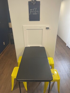 A room with a black table and yellow chairs, a white door, and a sign on the wall.