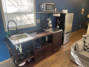 Uma cozinha compacta com pia, micro-ondas, cafeteira e geladeira.