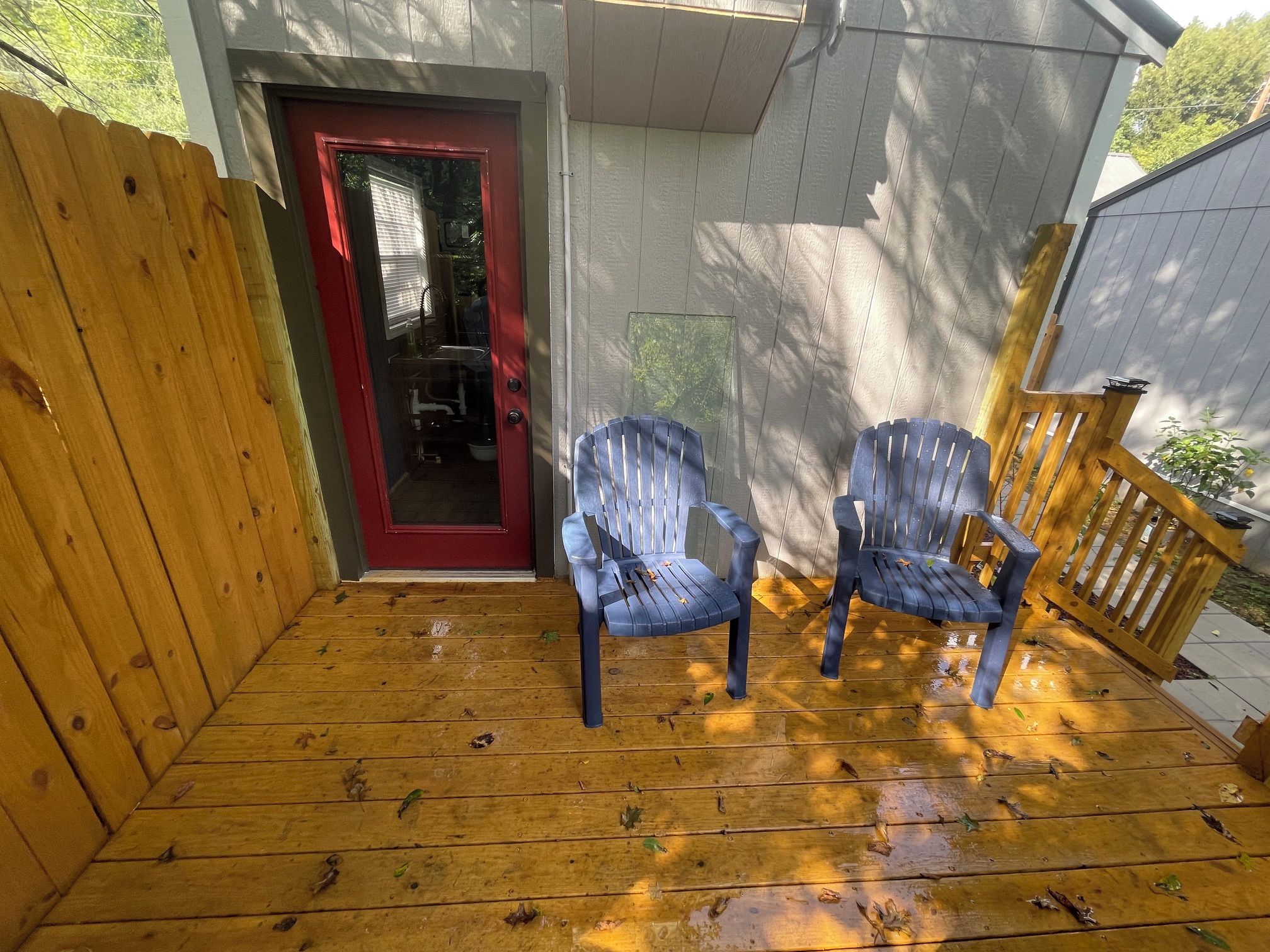 A wooden deck with two chairs and a red door leading to a covered area.
