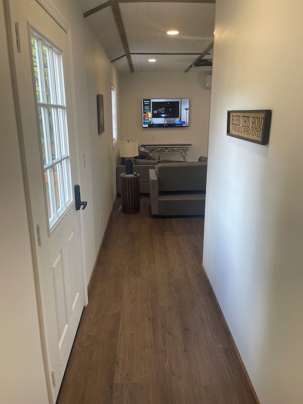 A hallway with a door, a window, a television mounted on the wall, and a sign on the wall.