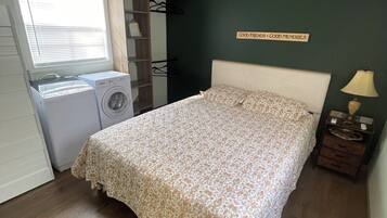 Une chambre avec un lit, un lave-linge, un étendoir et un radiateur fixé au mur.