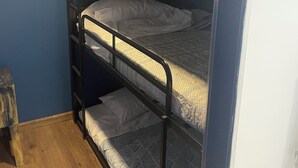 En våningssäng med en trästege, en mönstrad madrass och en enkel vägg.