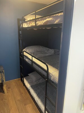 Uma cama de beliche com escada de madeira, colchão estampado e parede lisa.