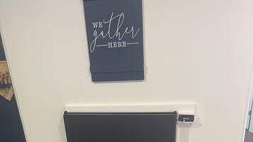 A room with a dark-colored wall, a sign that reads 'WE gather HERE', and two yellow stools.
