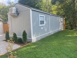 A single-story, gray mobile home with a small front yard, a window, and an air conditioning unit.