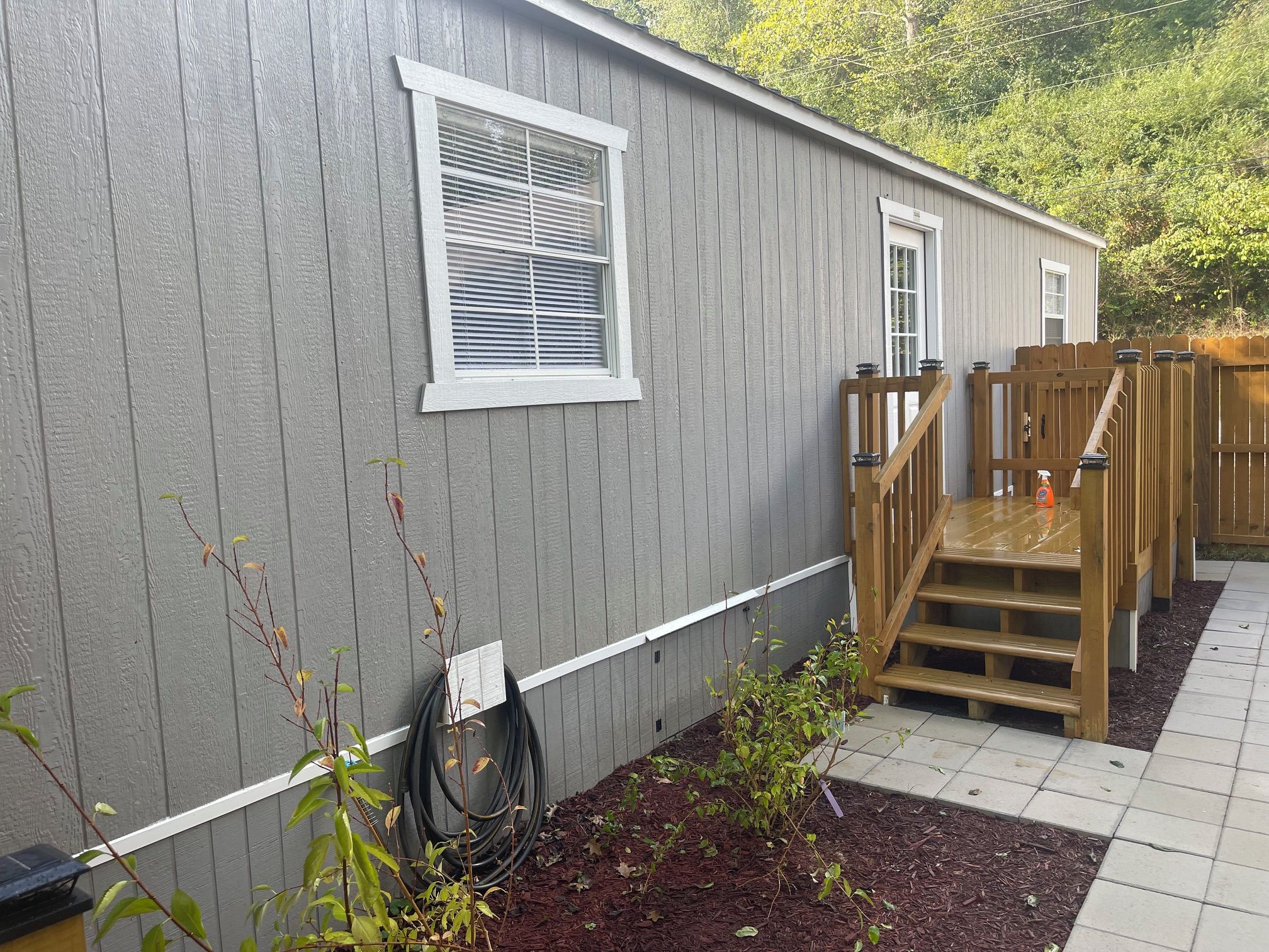 A single-story building with a covered outdoor area, a wooden staircase, and a garden bed with mulch.