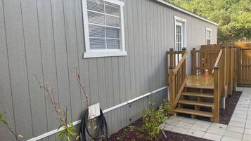 A single-story building with a covered outdoor area, a wooden staircase, and a garden bed with mulch.