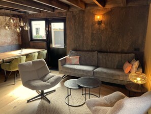 A cozy living area with a sofa, armchair, and round coffee table, a wooden dining table with chairs, and a wall-mounted lamp. - Schoorl Villa With Fireplace (Schoorl)