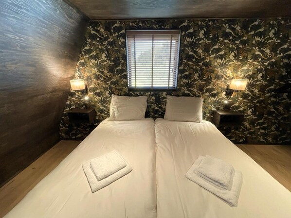 Een kamer met twee bedden, een raam met zonwering en wandlampen.