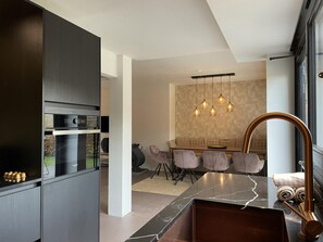 A modern kitchen with built-in appliances, a dining area with a marble countertop, and a unique curved faucet. - Schoorl Villa With Fireplace (Schoorl)