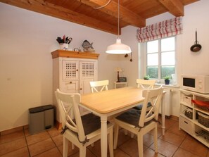 A dining area with a wooden table and white chairs, a white cabinet with a window, a microwave, and a window with a view of greenery. - Holiday Home With 1 Bedroom (Wrixum)