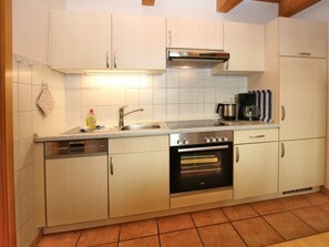Una cocina con armarios blancos, un lavamanos de acero inoxidable, un horno empotrado y una cafetera.