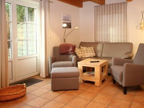 A living room with a sofa, ottoman, and a small wooden table with a remote control on it. - Holiday Home With 1 Bedroom (Wrixum)