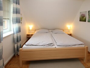 A single bed with a wooden frame, two bedside tables with lamps, a window with blinds, and a wall with a framed picture. - Holiday Home With 1 Bedroom (Wrixum)