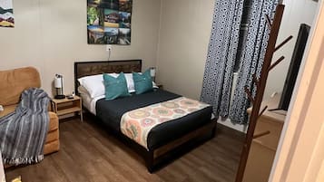 Ein Schlafzimmer mit einem Bett, einem Nachttisch, einer Lampe, einem Wandbild und einem gemusterten Vorhang.