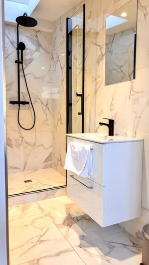 Ein modernes Badezimmer mit einer gläsernen Duschkabine, einem weißen Waschtisch mit schwarzem Wasserhahn und Wänden mit Marmoroptik.