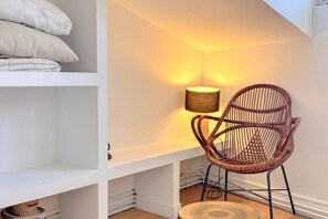 A room with a wicker chair, a lamp, and a white shelf with folded blankets. - Cosy Escape with A/C in Old Town (Bordeaux)