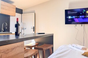 A modern hotel room with a wooden bar area, a television mounted on the wall, and a bed with towels. - Cosy Escape with A/C in Old Town (Bordeaux)